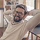 Mi primer trabajo - Chico joven con gafas sonriendo sentado en una silla en la biblioteca mientras estudia Mi primer trabajo - Chico joven con gafas sonriendo sentado en una silla en la biblioteca mientras estudia