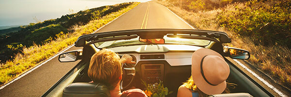Seguro del Automóvil - Pareja feliz conduciendo por la carretera con su coche descapotable Seguro del Automóvil - Pareja feliz conduciendo por la carretera con su coche descapotable