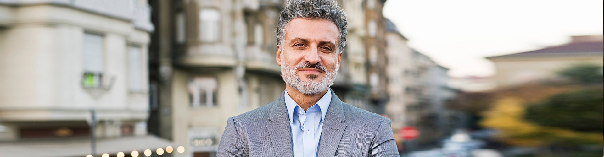 Cuentas a la Vista - Hombre de negocios con traje y smartwatch con los brazos cruzados en una ciudad Cuentas a la Vista - Hombre de negocios con traje y smartwatch con los brazos cruzados en una ciudad