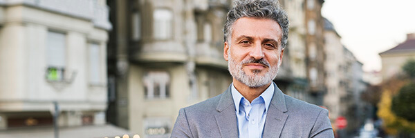 Cuentas a la Vista - Hombre de negocios con traje y smartwatch con los brazos cruzados en una ciudad Cuentas a la Vista - Hombre de negocios con traje y smartwatch con los brazos cruzados en una ciudad