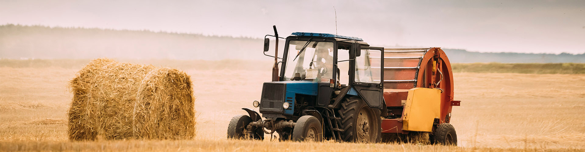 Seguros Agrarios - Tractor azul en el campo recogiendo paja para dar de comer al ganado Seguros Agrarios - Tractor azul en el campo recogiendo paja para dar de comer al ganado