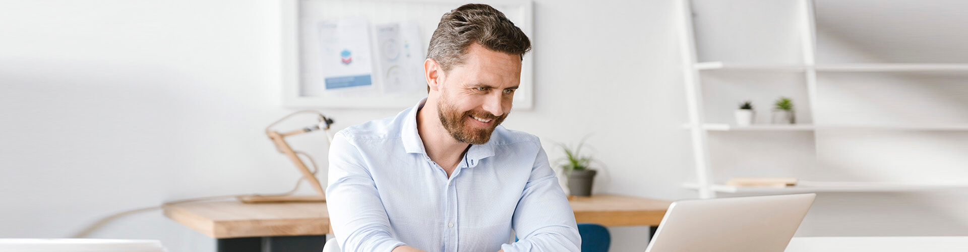 Servicios para tu gestión diaria Empresas - Hombre de negocios con camisa y sonriendo mientras se encuentra trabajando con su portatil en la oficina Servicios para tu gestión diaria Empresas - Hombre de negocios con camisa y sonriendo mientras se encuentra trabajando con su portatil en la oficina