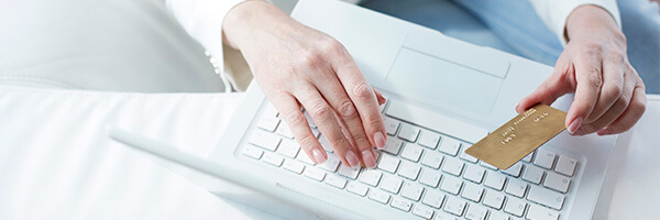 TPV Virtual - Mujer sentada en el sofa de su casa con su portatil pagando con una tarjeta en internet TPV Virtual - Mujer sentada en el sofa de su casa con su portatil pagando con una tarjeta en internet