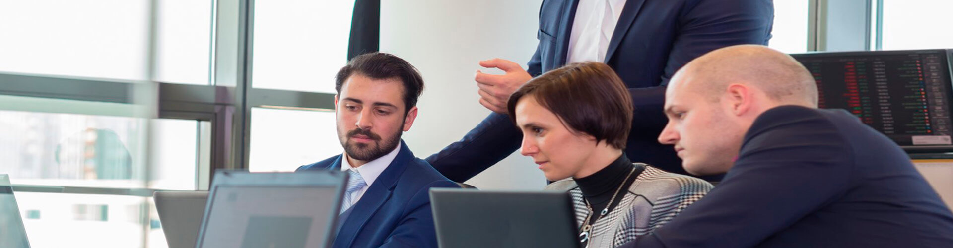 Transferencias y ordenes de pago para empresas - Varias personas trajeadas reunidas, mirando los portátiles en la oficina Transferencias y ordenes de pago para empresas - Varias personas trajeadas reunidas, mirando los portátiles en la oficina