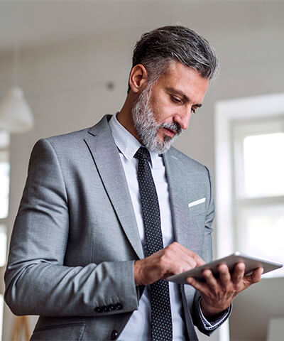 Momento Digitalizar mis gestiones- Hombre de mediana edad con barba, traje gris y corbata negra trabajado en la oficina con una tablet pensando en digitalizar las gestiones de su empresa Momento Digitalizar mis gestiones- Hombre de mediana edad con barba, traje gris y corbata negra trabajado en la oficina con una tablet pensando en digitalizar las gestiones de su empresa