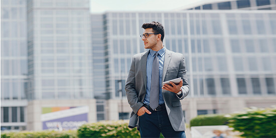 Promocion Buzon Virtual - Hombre de negocios con traje y corbata andando por la calle de la ciudad con un movil en la mano Promocion Buzon Virtual - Hombre de negocios con traje y corbata andando por la calle de la ciudad con un movil en la mano