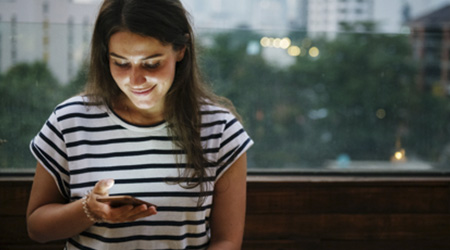 Ruralvía móvil - Chica con camiseta de rayas con su móvil en la mano sonriendo