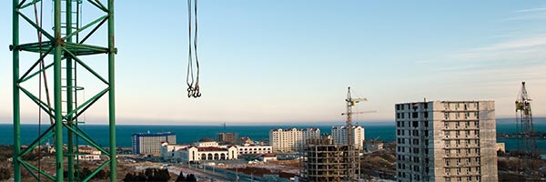 Seguro Decenal de Daños - Obra construyendo edificios con gruas, camiones y trabajadores trabajando Seguro Decenal de Daños - Obra construyendo edificios con gruas, camiones y trabajadores trabajando