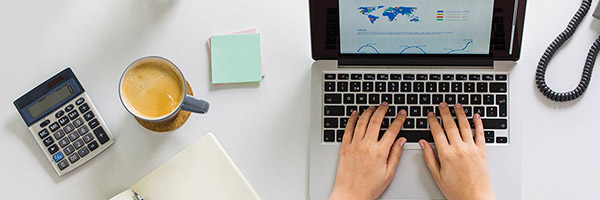Operaciones en divisas - Persona trabajando en su portátil con un café, una calculadora y un teléfono Operaciones en divisas - Persona trabajando en su portátil con un café, una calculadora y un teléfono