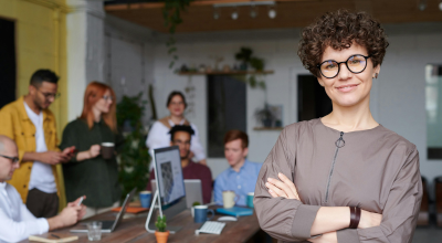 Primer plano de mujer con los brazos cruzados con sus compañeros de trabajo detrás