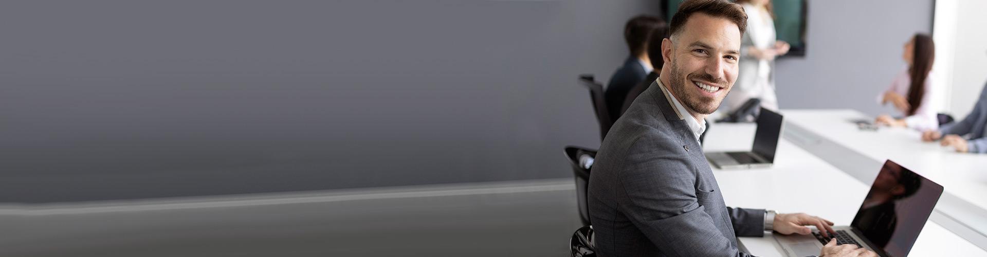 Empresas - Hombre de traje sonriendo sentado junto a su portatil en una sala de reuniones en la oficina