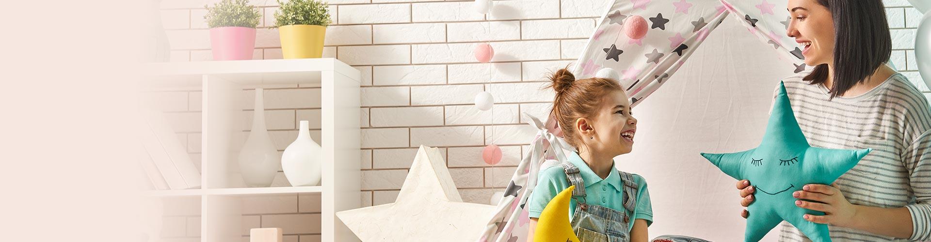 Particulares Prestamos Personales - Madre e hija sentadas en el suelo de su casa sonriendo jugando con peluches con una tienda de indio de fondo