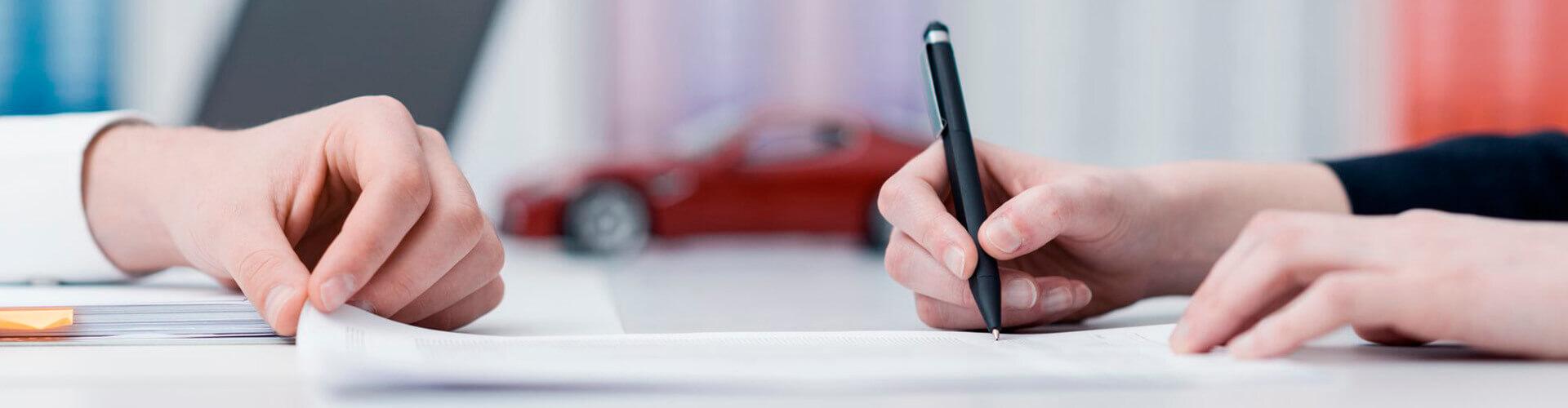 Rural Renting de Automoción y Equipamientos empresas - Manos firmando un contrato en la oficina con un coche de fondo