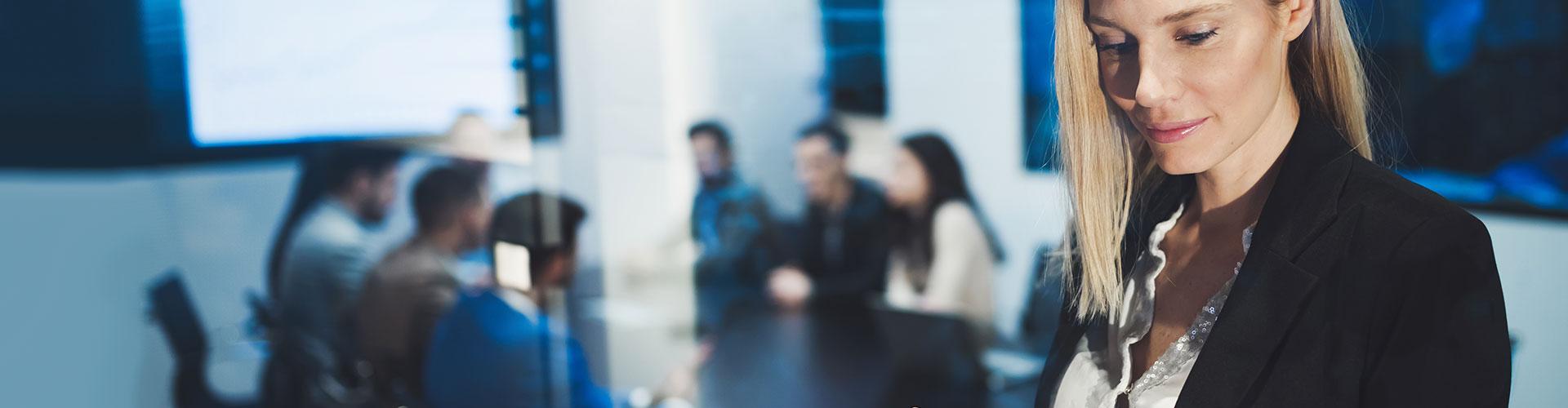 Seguros para Empresas - Mujer joven y rubia de negocios con chaqueta de traje negra y camisa blanca utilizando una tablet en una reunion en la oficina