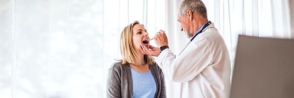 Seguro de Salud - Doctor senior examinando a una joven mujer en su consulta médica