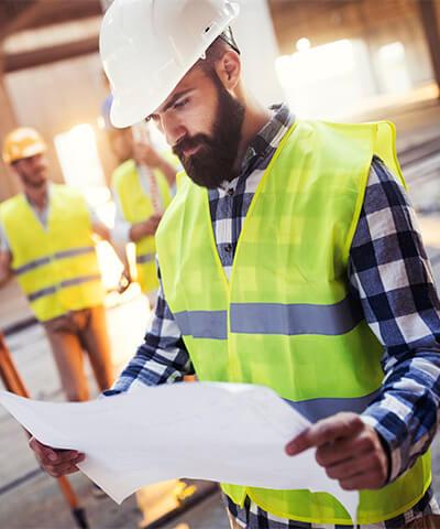 Ventajas para Seguro de Responsabilidad Civil Autonomos - Ingeniero con casco blanco, chaleco reflectante y camisa de cuadros azules mirando un plano en una obra