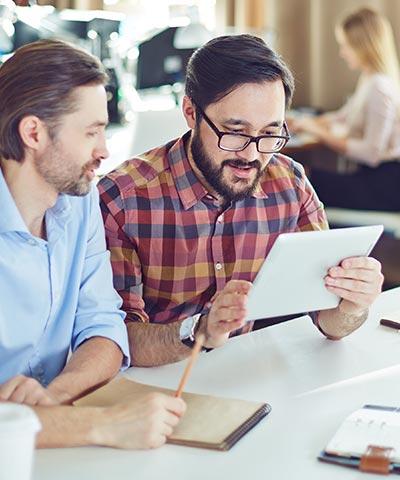 Seguros Colectivos para Empleados - Dos trabajadores con camisa trabajando en la oficina con su tablet